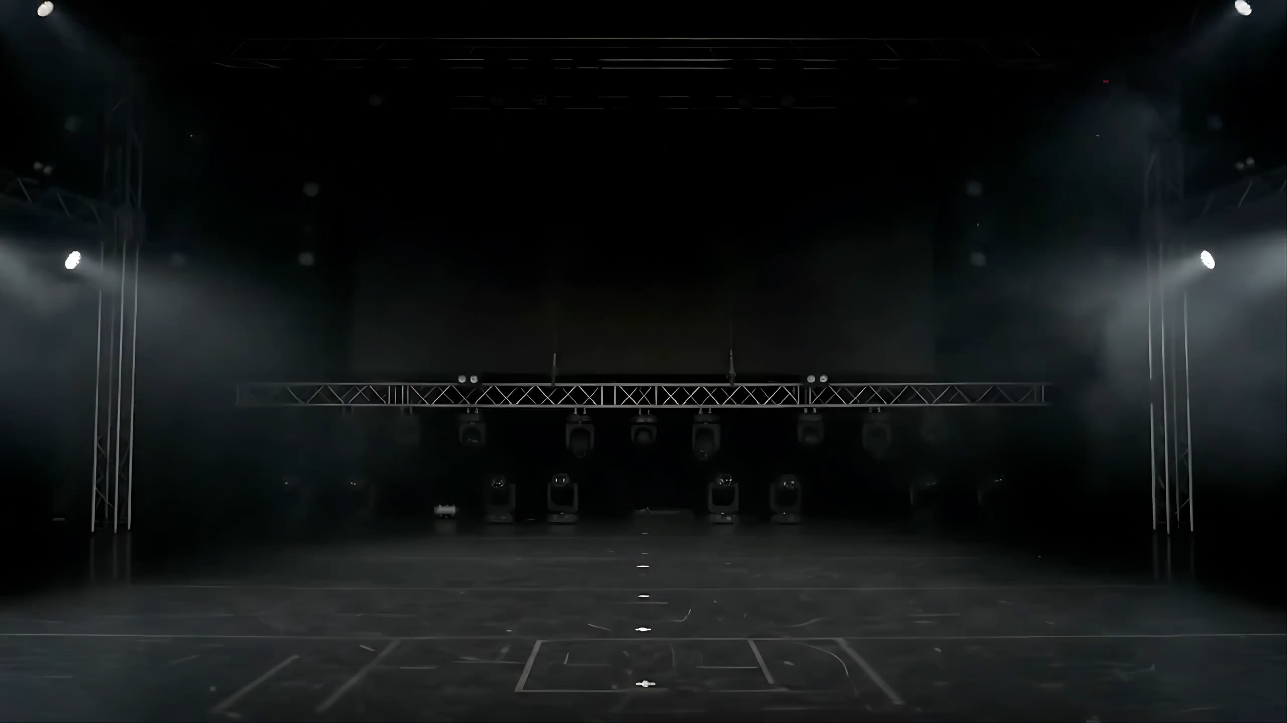 A dark stage lit by converging beams over a production floor.